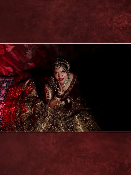 An artistic, wide-angle shot of the bride looking up at the camera, surrounded by the rich fabric of her lehenga.