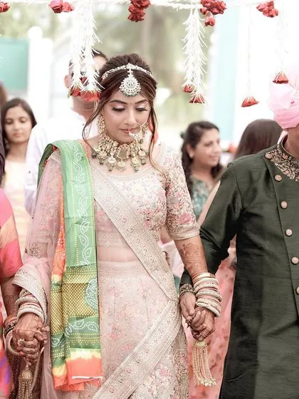 The bride's grand entrance, walking under a phoolon ki chadar held by her family. This shot captures the emotional moment as she is escorted by her parents to the wedding mandap.