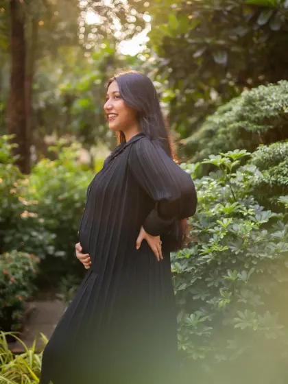 The expecting mother is captured in beautiful side-profile light, smiling as she looks into the distance. This shot highlights her happy glow against a garden backdrop.