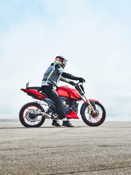 A stunt rider on a red bike, surrounded by smoke. The hazy, atmospheric shot captures the gritty, raw energy of the stunt arena.