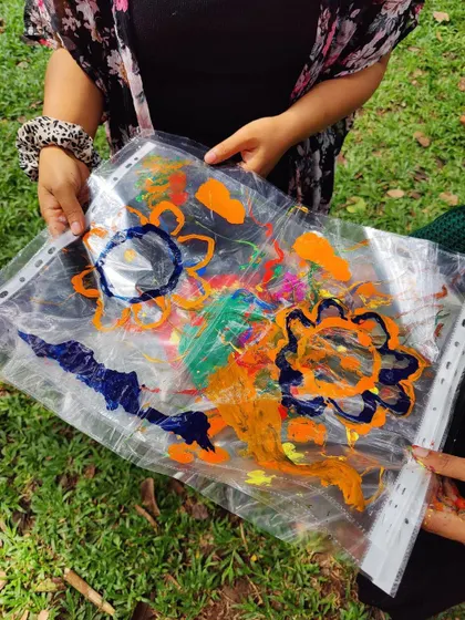 A participant showing off a beautiful, colorful piece created on a transparent sheet, with the park's greenery in the background.