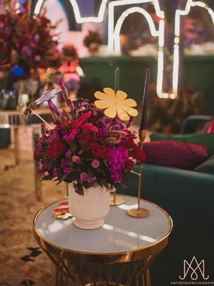 A vibrant centerpiece with red and purple flowers on a modern gold and white table, with fun paper flower cutouts adding a playful element.