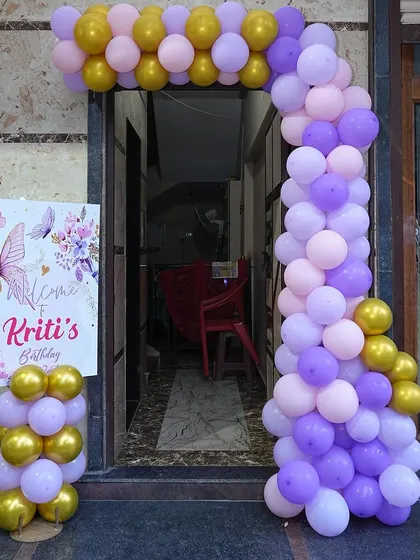 An L-shaped entrance arch is a great way to decorate a corner entryway. This one, for a butterfly-themed party, uses purple, pink, and gold balloons and includes a welcome board.