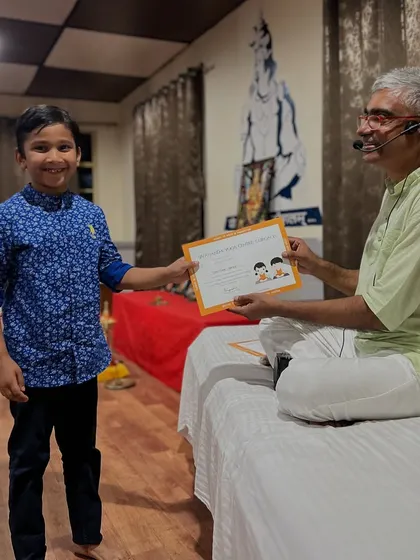 A smiling young graduate receives his certificate after a week of fun, learning, and making new friends at the Kids and Parents Yoga Retreat.
