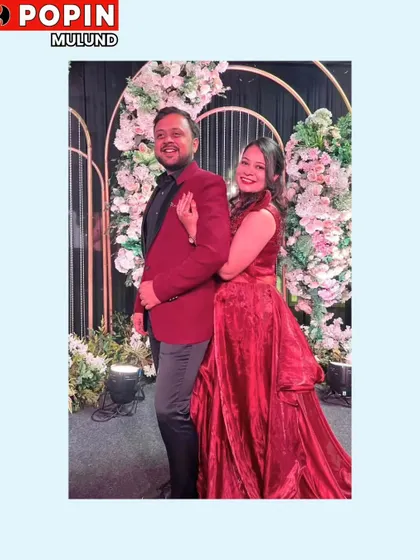 A couple dressed in red and black for their special day. He wears a sharp maroon blazer that coordinates perfectly with her flowing red gown.