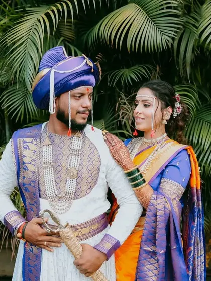 A full-length portrait of the couple in their royal blue and orange wedding outfits, looking like Maharashtrian royalty.