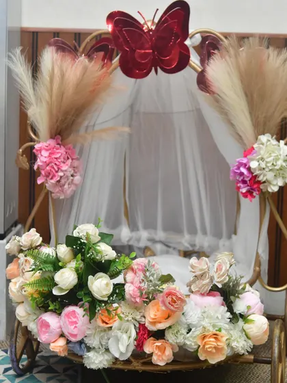 This decorated cart is another wonderful option for a baby's grand entrance. It's adorned with flowers, pampas grass, and a sheer canopy for a royal feel.