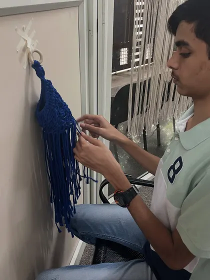 A student works on his blue macrame plant hanger. This project is not only creative but also results in a beautiful and functional item for the home.