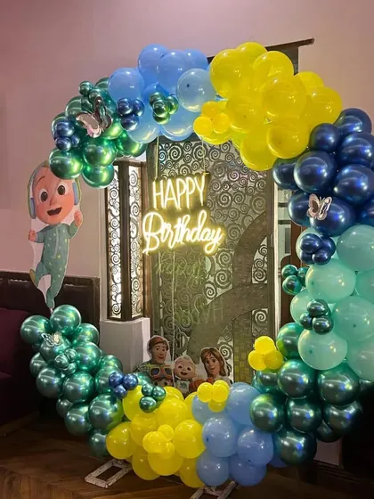 A Cocomelon themed birthday party with a circular balloon arch and a 'Happy Birthday' neon sign.