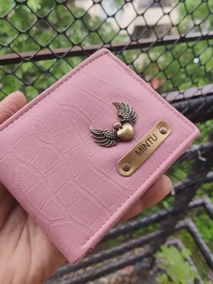 A pink crocodile-textured wallet personalized with a name and a heart-with-wings charm. This shows a softer, more feminine customization option.