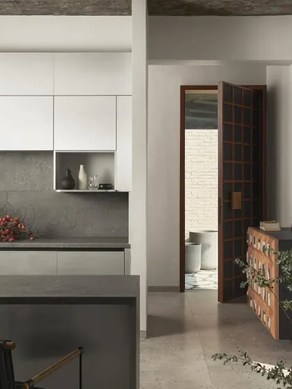 The open kitchen at Pavilion House, with its minimalist white cabinets and dark stone countertops, looks out onto the living area and the landscape beyond.