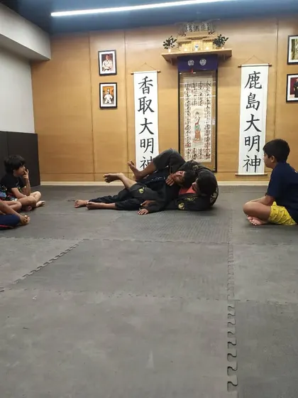 A kids' BJJ class watching a demonstration. It's important for them to see the techniques applied correctly before they practice.