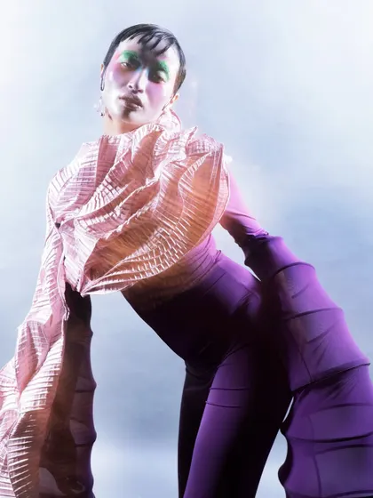 A tilted close-up that highlights the textured pink fabric and the model's expressive, artistic makeup. The angle and soft lighting create a disorienting yet captivating perspective on the abstract form.