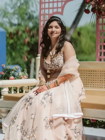 A serene portrait of the bride at her Mehendi. The pastel pink decor with delicate floral arrangements and cane furniture creates a soft, feminine, and relaxed ambiance.