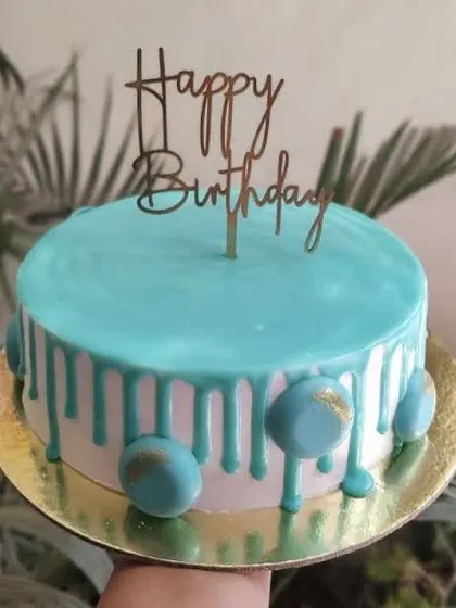 A modern take on a blue drip cake, decorated with matching chocolate spheres and a simple "Happy Birthday" topper.