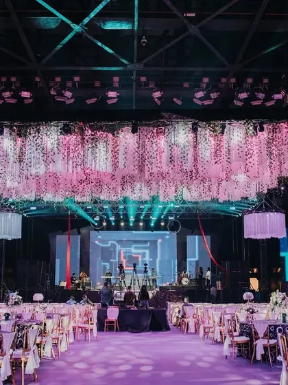 A grand overview of Tanisha and Neel's psychedelic-themed Sangeet. The space is dominated by a massive floral and fringe installation hanging from the ceiling, with vibrant pink lighting and modern lounge seating below.