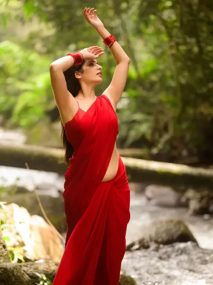 An expressive outdoor shot of actress Thejaswini Sharma. Her pose, reaching towards the sky, combined with the natural setting, evokes a sense of freedom and connection with the environment.