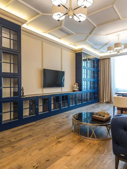 A luxurious living room design featuring deep blue, floor-to-ceiling cabinetry with glass doors, a matching blue tufted sofa, and a geometric coffered ceiling for a touch of grandeur.