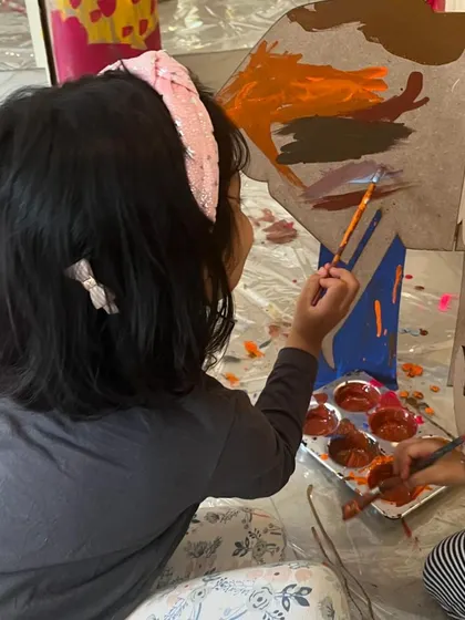 A young artist concentrates on painting a large cardboard elephant. We provide a variety of materials and scales to work on, allowing children to experience art in different ways.