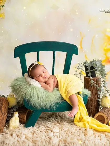 I use a variety of props and setups to create unique portraits. This baby is posed sweetly on a miniature chair, surrounded by a cheerful yellow floral theme, showing a different style of posed newborn photography.