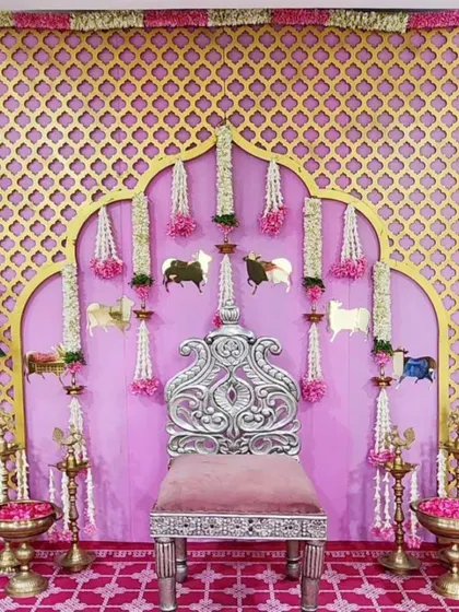 A beautiful baby shower setup featuring a pink and gold lattice backdrop. The decor is accented with traditional cow motifs, floral garlands, and banana trees, perfect for a Godh Bharai ceremony.