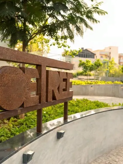 A close-up of the POETREE entrance signage, showcasing the raw texture of the corten steel against the soft backdrop of the surrounding landscape.