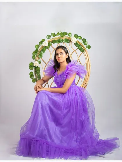 A model seated in a peacock chair, wearing the lavender ruffled gown. This shows how versatile the gown is for different photoshoot setups.