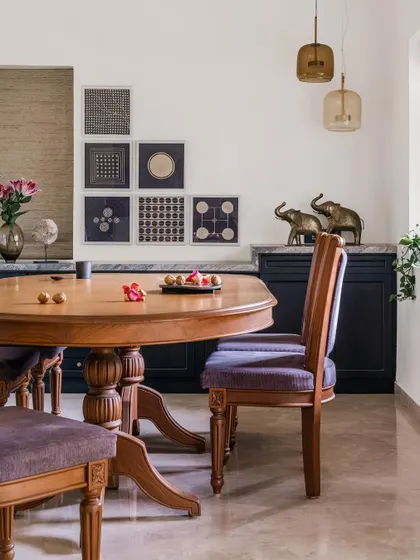 The dining area in Relic House exudes vintage charm with its intricately carved wooden table and chairs upholstered in a deep purple fabric. We curated a gallery wall of block-print art and added brass elephant figurines to complete this elegant, culturally rich space.