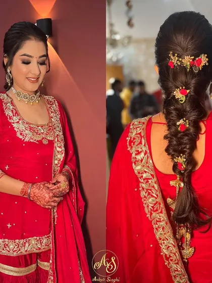 A beautiful engagement look featuring a classic braid with a twist. The hair is styled in a voluminous braid and decorated with delicate red floral accessories, adding a pop of color to her red sharara suit.