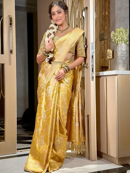 A full-length portrait of the South Indian bride, looking like a goddess in her golden saree. The makeup is kept luminous and warm to complement the traditional attire and intricate jewelry.