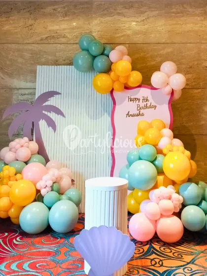A pastel-colored balloon arrangement with a palm tree cutout, creating a chic and tropical photo corner for a pool party.