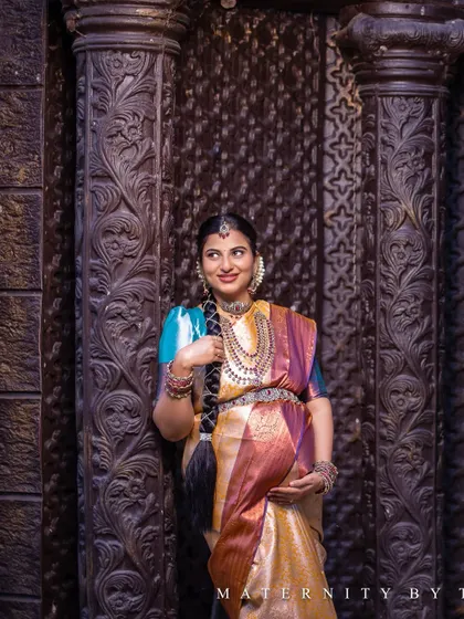 Posed against a beautifully carved wooden pillar, the mother-to-be looks radiant. This location in Chennai provides a perfect backdrop for traditional maternity photos, blending culture with natural beauty.