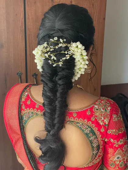 A beautiful fishtail braid paired with a traditional red and green saree. The braid is decorated with fresh jasmine flowers and a gold accessory.