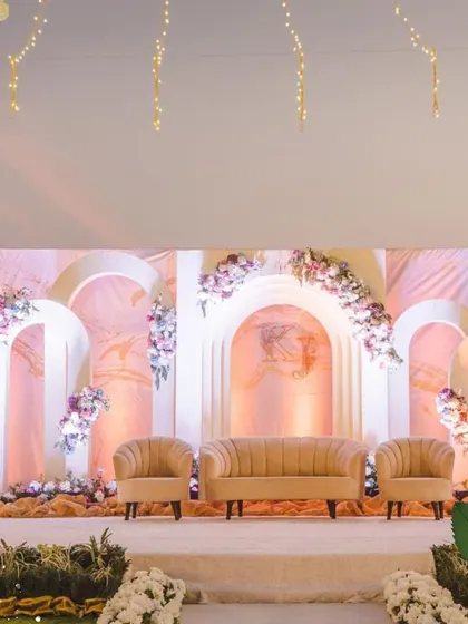 A beautiful and modern stage backdrop with clean arches and asymmetrical floral arrangements. The soft, warm lighting creates a romantic and inviting focal point.