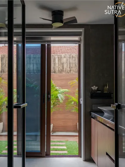 Another perspective of the bathroom that opens to a private green space. The dark-toned tiles and wooden vanity create a moody, sophisticated atmosphere that is balanced by the freshness of the outdoor view.