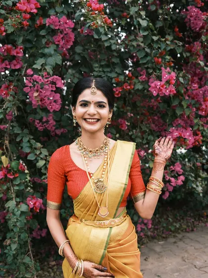 A happy bride in a mustard yellow silk saree. Her makeup is classic and timeless, with a red lip and defined eyes that complement her traditional gold jewellery.