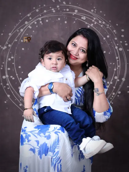 A loving mother holds her baby boy, both dressed in coordinating white and blue outfits. The soft, artistic background adds a touch of elegance to this beautiful mother-son portrait.