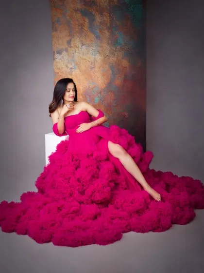 A relaxed, reclining pose that still feels incredibly glamorous. The voluminous magenta gown creates a stunning visual against the artistic, textured backdrop.
