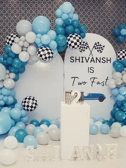 A sleek and modern take on a car theme for Shivansh's second birthday. This "Two Fast" setup features a clean white backdrop with a blue balloon arch and checkered flag balloon accents for a cool, race-inspired look.