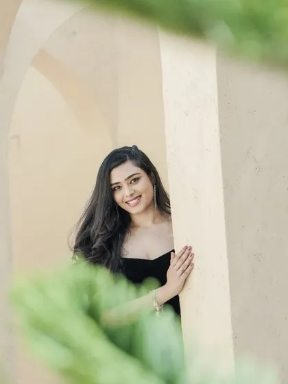 A candid, peeking portrait of the bride-to-be, her smile captured through a gap in the foliage, adding a touch of mystery and charm.
