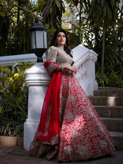 A full length portrait of Mahima against a white staircase. Her makeup is classic and timeless, perfectly complementing her regal pose and stunning lehenga.