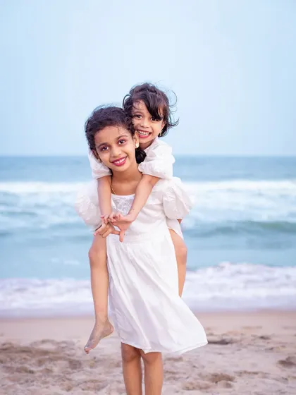 A sweet piggyback ride by the sea. This playful portrait of two sisters showcases their loving bond and the simple joys of a day spent at the beach, creating a cherished memory for their family.