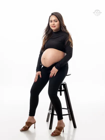 A confident and stylish portrait of a mom-to-be in a modern all-black outfit, seated on a stool.