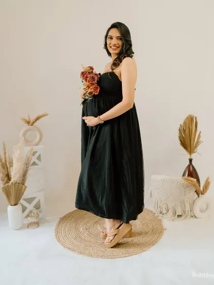 A happy and glowing portrait in a simple black dress, holding a bouquet of rustic flowers. The bohemian-style props add a warm and trendy touch to the studio setup.