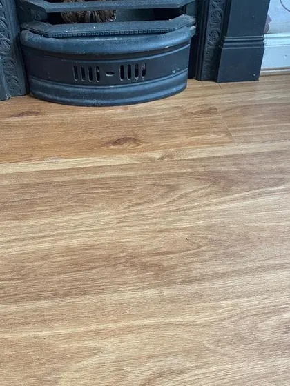 This close-up shows the natural texture of a light oak laminate floor installed near a traditional fireplace. It's a practical and stylish choice that brings the look of real wood with added durability.