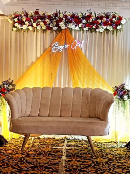 A simple floral decoration for a baby shower. The setup includes floral pillars, a "Boy or Girl" neon sign, and a modern sofa, creating a clean and stylish look for a gender reveal party.