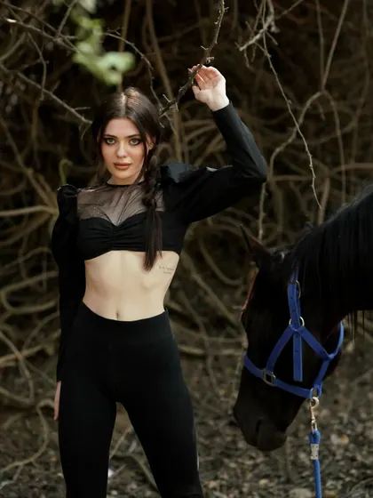 A model poses with a black horse against a backdrop of tangled branches, creating a raw and mysterious atmosphere. Our varied landscapes include wooded areas for more dramatic shoots.