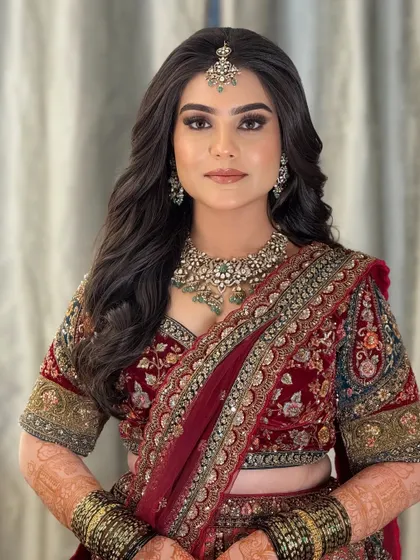 A stunning reception look in a deep red velvet lehenga. The makeup is glamorous and bold, with a smoky eye and a defined brow.