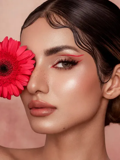A study in graphic lines and floral elements. The sharp red eyeliner is mirrored by the vibrant gerbera daisy, creating a visually balanced and artistic composition. The finger-waved hair adds a touch of vintage glamour to this modern look.