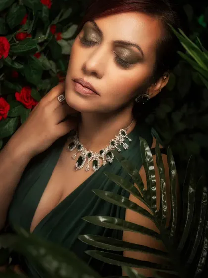 A close-up portrait set in a lush, green environment created with a combination of real and projected foliage. The soft lighting beautifully highlights the model's features and the delicate jewelry.